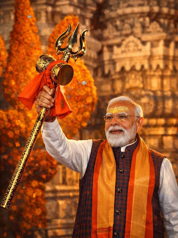 Primo piano di Narendra Modi con scettro dorato e corona, davanti a sfondo di tempio e fiori arancioni. Brics